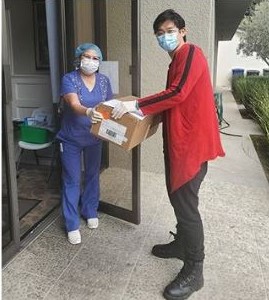 student, wearing a covid-19 mask and gloves, delivering boxes of face masks to the front door of a senior center.